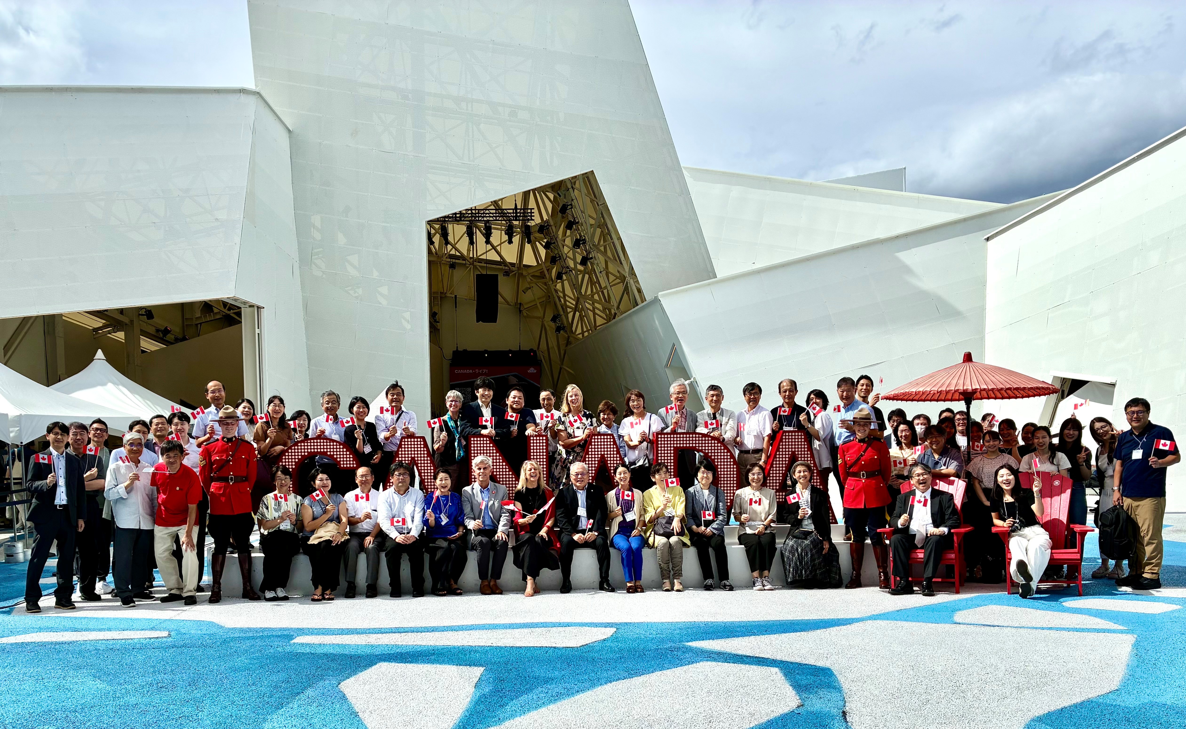 Group photo of JACS conference attendees in front of the Canada Pavilion with two Royal Canadian Mounted Police officers Photo de groupe devant le pavillon du Canada avec deux agents de la Gendarmerie royale du Canada